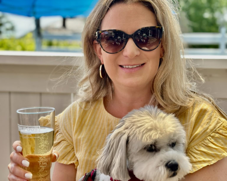 Woman enjoying sunny day with a dog, beer, and nature.