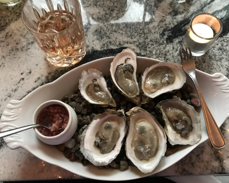 Luxurious seafood platter with fresh oysters, sauce, drink, and candlelight ambiance.