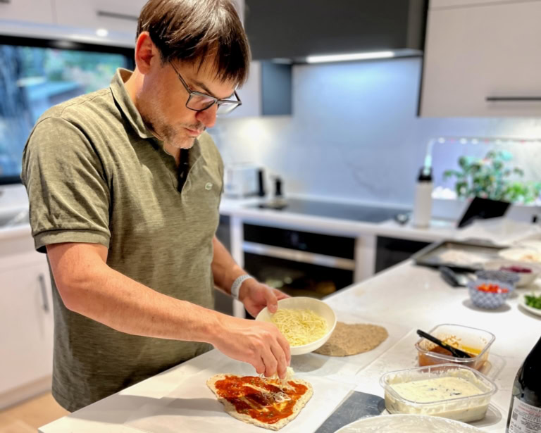 Man making homemade pizza in modern kitchen with fresh ingredients and organized countertop.
