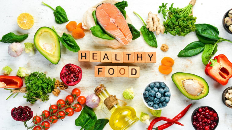 Healthy foods featuring salmon, avocado, greens, and fruits for balanced nutrition.