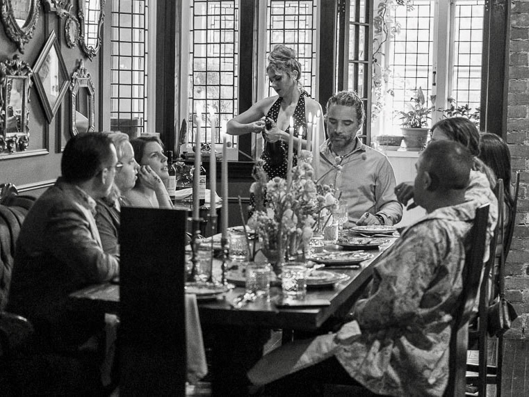 Elegant dinner scene with diverse guests, candlelight, fresh flowers, and a poised waitress.