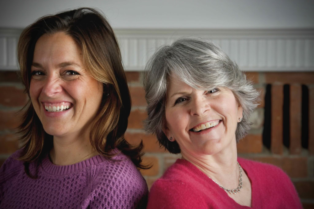 Friendly women smiling together, supporting home cooking and food blog with a brick background.