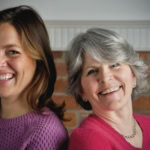 Friendly women smiling together, supporting home cooking and food blog with a brick background.