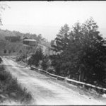 Black and white photo of a peaceful rural scene with dirt road, trees, and hillside houses.
