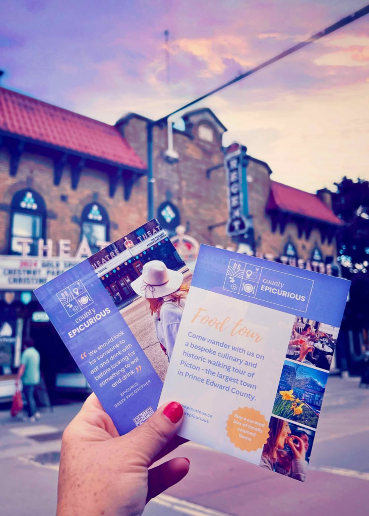 Hand holding food tour flyers outside a historic theatre in Prince Edward County.