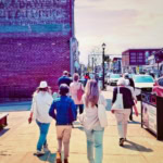 Vintage-inspired image of pedestrians strolling through a lively downtown shopping district on a sunny day, highlighting local businesses and community atmosphere.