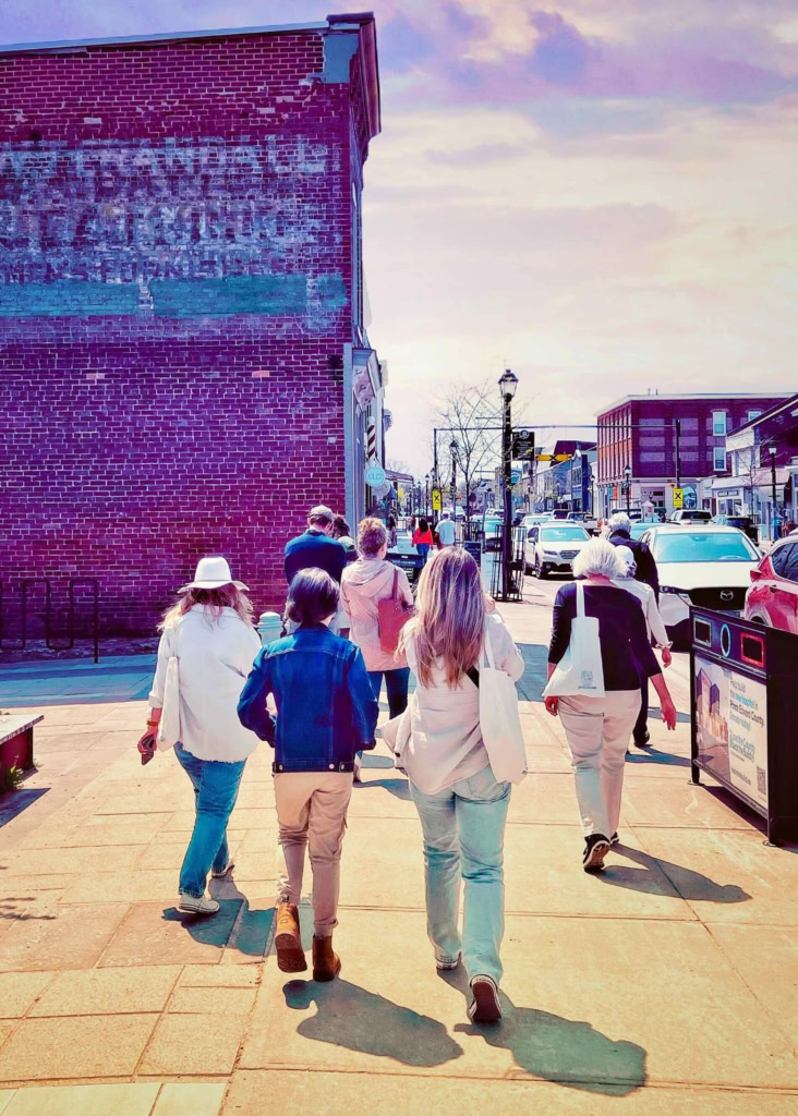 Vintage-inspired image of pedestrians strolling through a lively downtown shopping district on a sunny day, highlighting local businesses and community atmosphere.