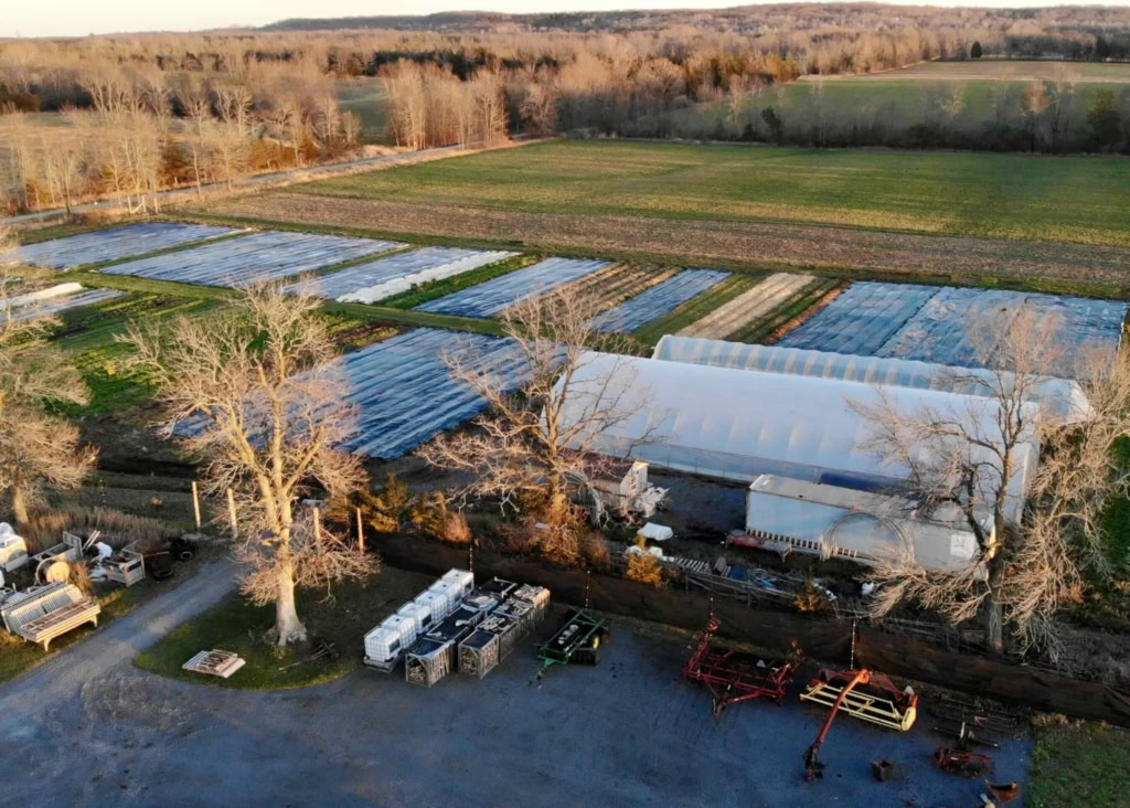 Aerial view of a rural farm with greenhouses and surrounding fields, showcasing sustainable farming at The Gourmet Host.