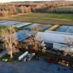 Aerial view of a rural farm with greenhouses and surrounding fields, showcasing sustainable farming at The Gourmet Host.