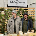 Vibrant farm stand showcasing Edwin County Farms holiday wreaths and local maple syrup.