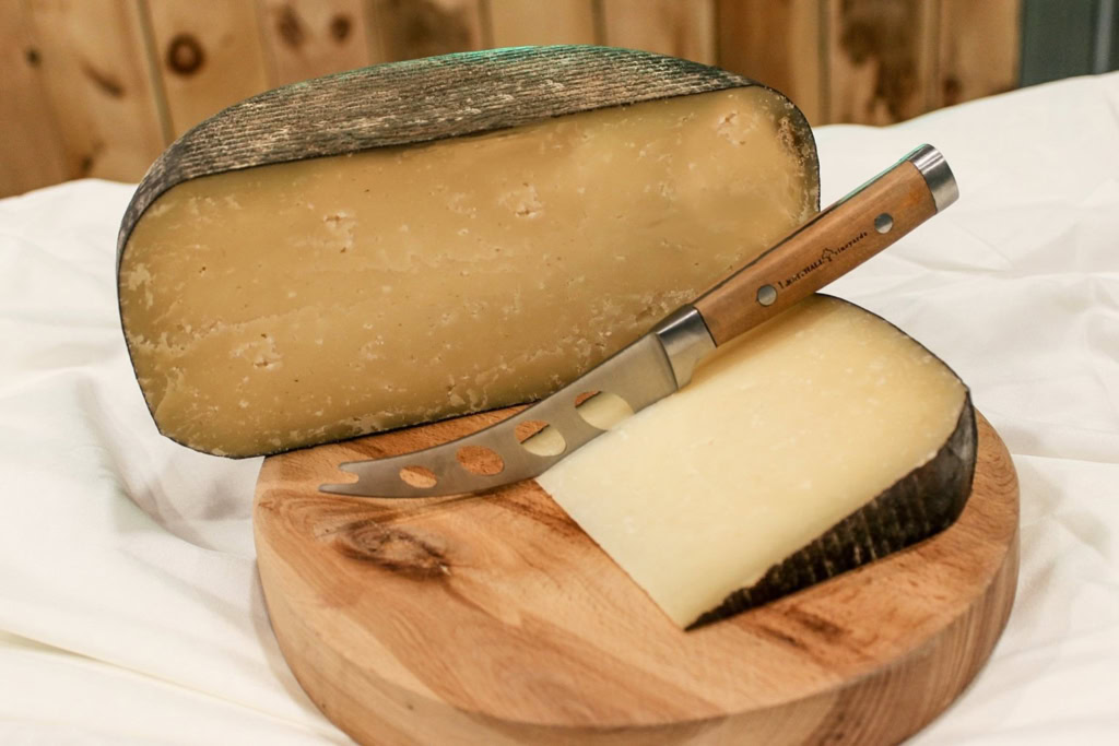 A close-up of aged cheese with a cheese knife on a wooden board, showcasing gourmet cheese platter, The Gourmet Host.