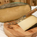 A close-up of aged cheese with a cheese knife on a wooden board, showcasing gourmet cheese platter, The Gourmet Host.