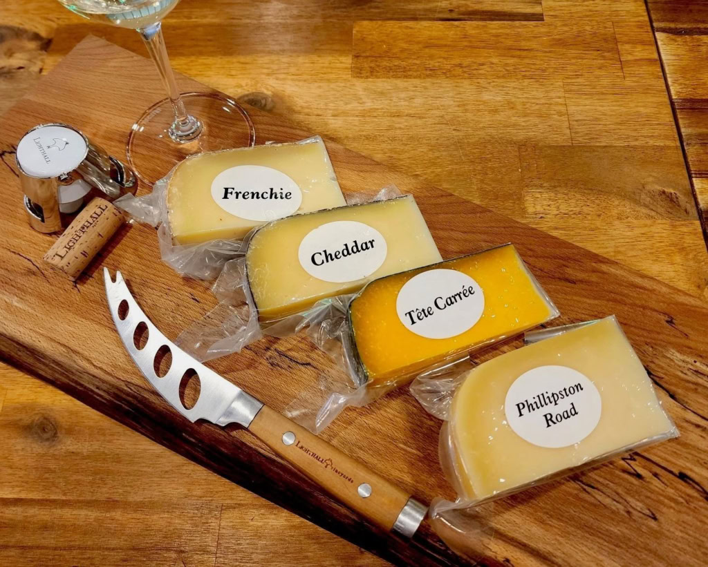 Assorted cheeses including Frenchie, Cheddar, and Tête Carrée on a wooden board, perfect for wine and cheese pairing.