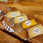 Assorted cheeses including Frenchie, Cheddar, and Tête Carrée on a wooden board, perfect for wine and cheese pairing.