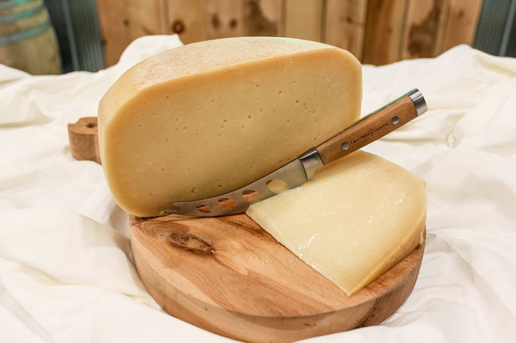 Fresh cheese wheel on wooden platter with a cheese knife, ideal for gourmet cheese tastings.