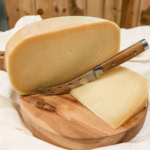 Fresh cheese wheel on wooden platter with a cheese knife, ideal for gourmet cheese tastings.