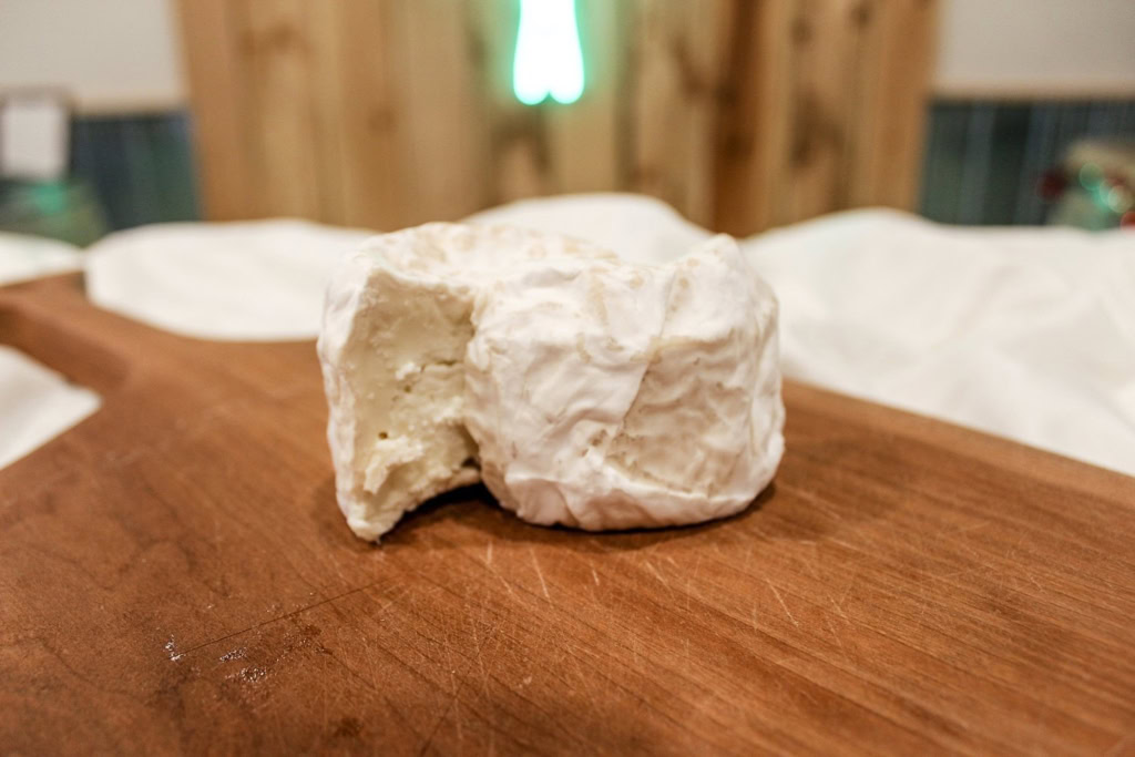 Close-up of a soft cheese wheel on a wooden cheese board, perfect for gourmet cheese tasting.