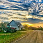 Old farm barn with tractor on rural road during sunset, beautiful sky and rural landscape.