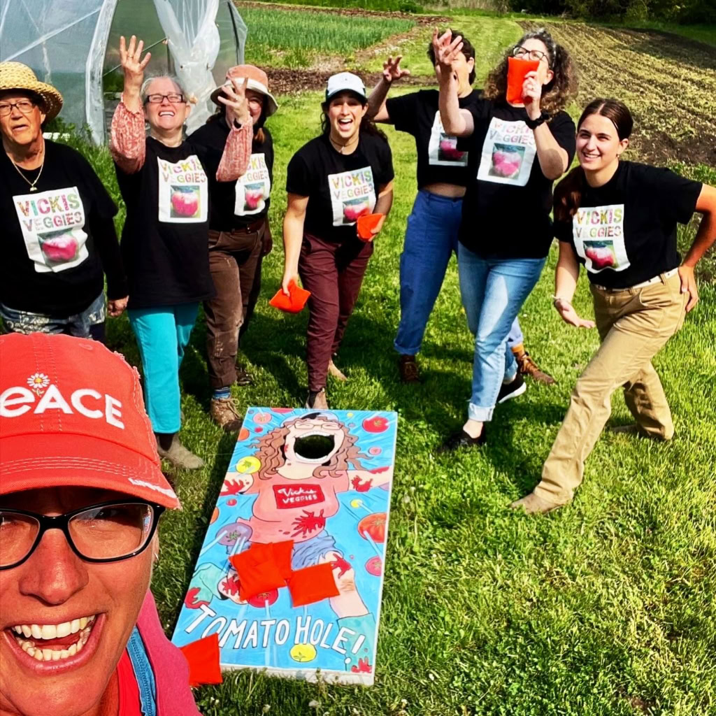 Vicki's Veggies team enjoying outdoor team-building activity on a lush farm, with vibrant green fields and a colorful game board, emphasizing fresh produce and farm-to-table experiences.