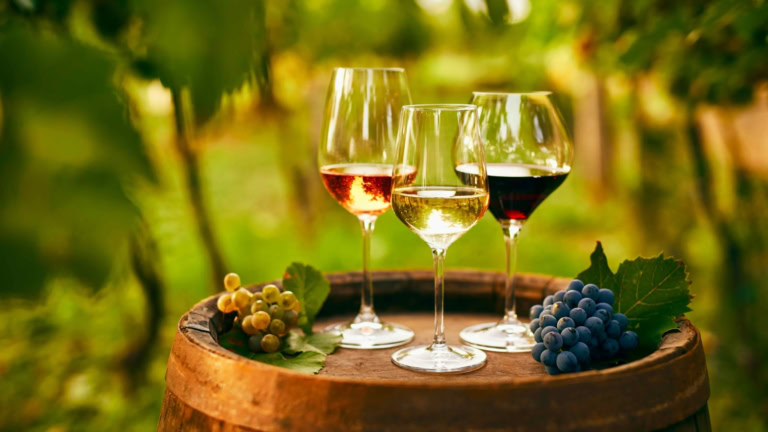 Wine glasses on rustic barrel with grapes in scenic vineyard setting.