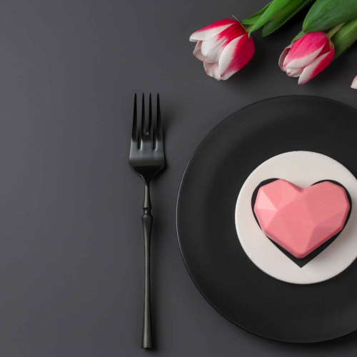 Heart-shaped cake with tulips on elegant table setting, perfect for romantic celebrations.