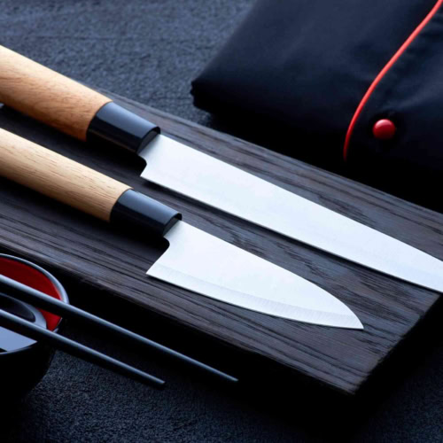 Japanese knives and chopsticks on dark cutting board showcasing culinary craftsmanship and Asian influences.