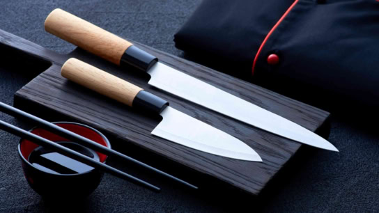 Japanese knives and chopsticks on dark cutting board showcasing culinary craftsmanship and Asian influences.