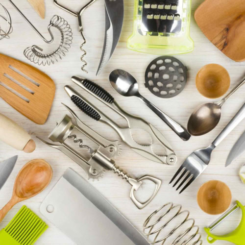 Assorted kitchen tools: wooden spoons, spatulas, wire whisk, corkscrew, grater, knives, green peeler.