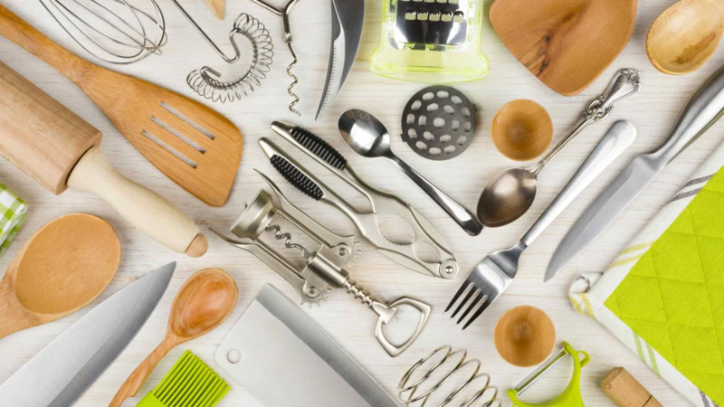 Assorted kitchen tools: wooden spoons, spatulas, wire whisk, corkscrew, grater, knives, green peeler.