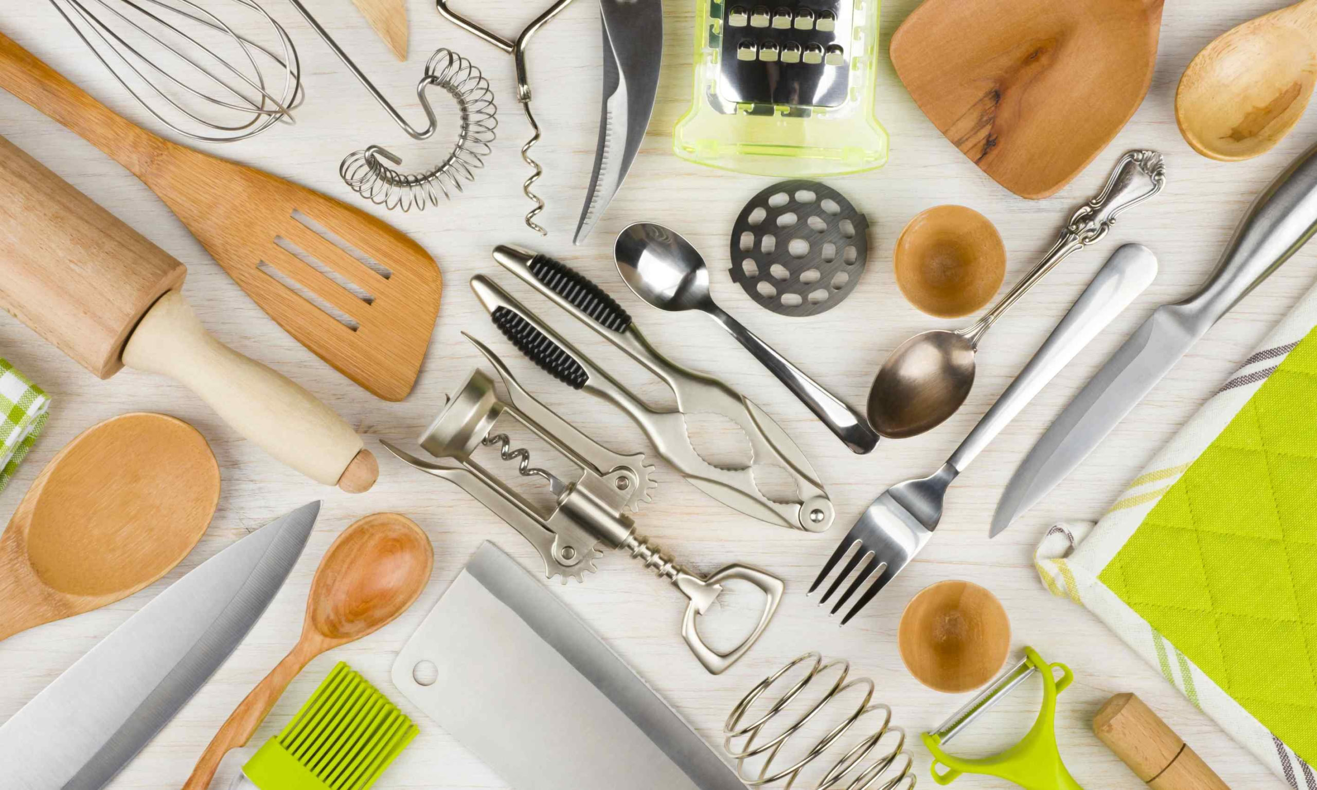 Assorted kitchen tools: wooden spoons, spatulas, wire whisk, corkscrew, grater, knives, green peeler.