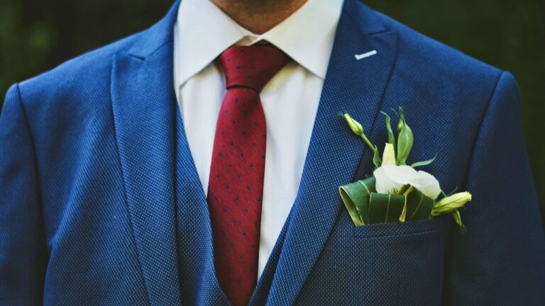 Groom wearing a navy suit with a white boutonniere and red tie, ready for his wedding speech.