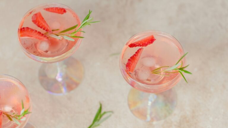 Elegant pink cocktail with strawberries and rosemary garnish in a glass.