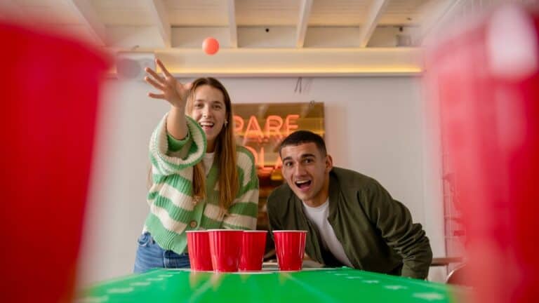 Two adults playing beer pong at a dinner party with friends.