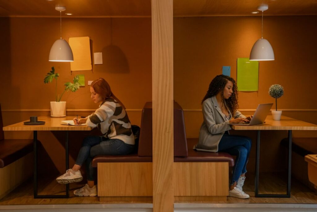 Cozy café workspace with women working independently on laptops, surrounded by warm, wooden accents.