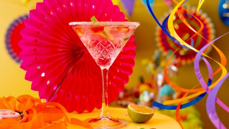 Festive party cocktail garnished with lime, colorful paper fans, and streamers for a fun dinner part.