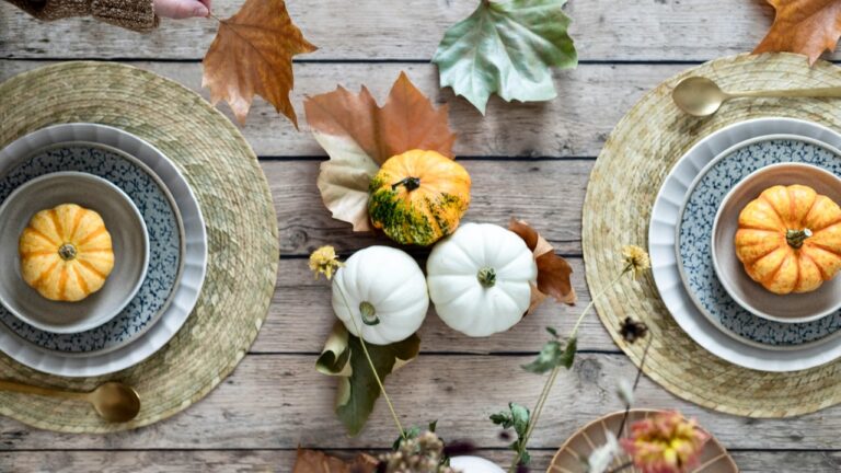 Elegant autumn-themed dinner table with pumpkins and fall leaves.
