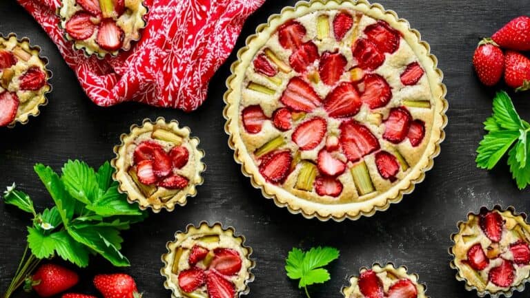 Fresh strawberry fruit tart with sliced strawberries and green mint leaves on a dark background.