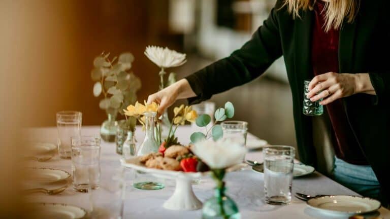 Brunch table with floral arrangements, food, and glassware for hosting a stylish gathering.