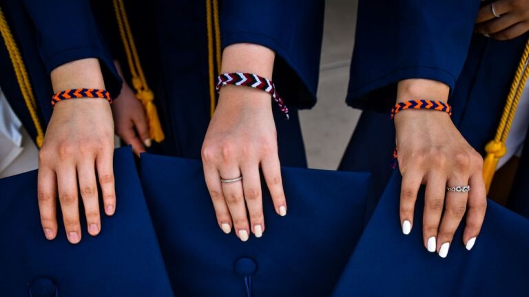 Elegant graduation table with hands displaying rings and bracelets, featuring navy blue gowns and ye.