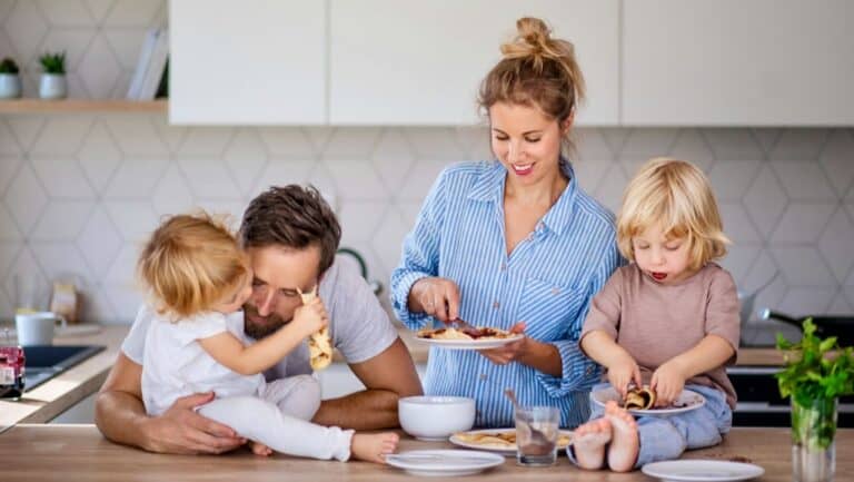 Happy family with two children sharing a meal in a bright, contemporary kitchen setting.