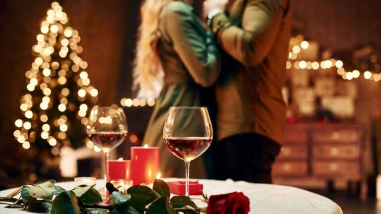 Elegant dinner setting for two with red wine, candles, and festive lights.