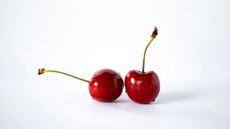 Fresh cherries with stems on a clean white background, highlighting quality and freshness.