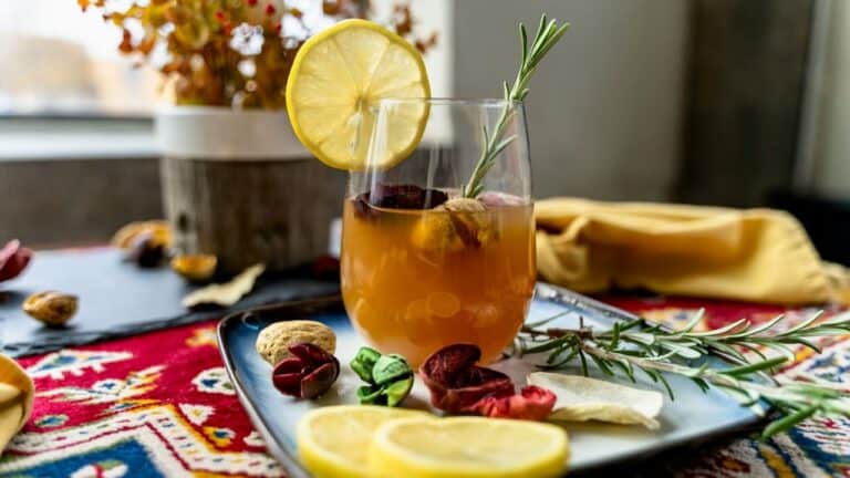 Non-alcoholic cocktail with lemon, herbs, and fruit garnishes on a colorful table.