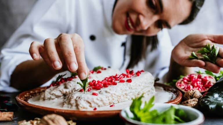 Gourmet chef garnishing a dish with fresh herbs and red berries for stunning presentation.