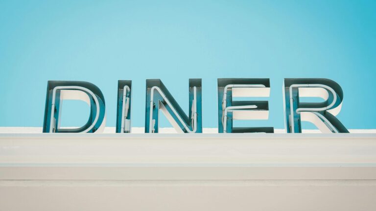 Diner sign with illuminated letters on a bright blue sky background.