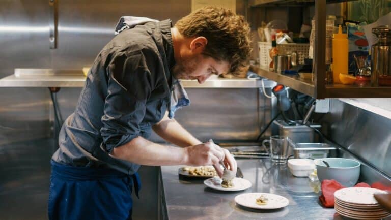 Chef plating a sophisticated dish with attention to detail in a modern kitchen setting.