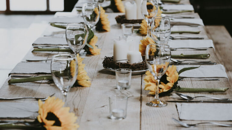 Elegant table setting with sunflowers, candles, and glassware for hosting a party.
