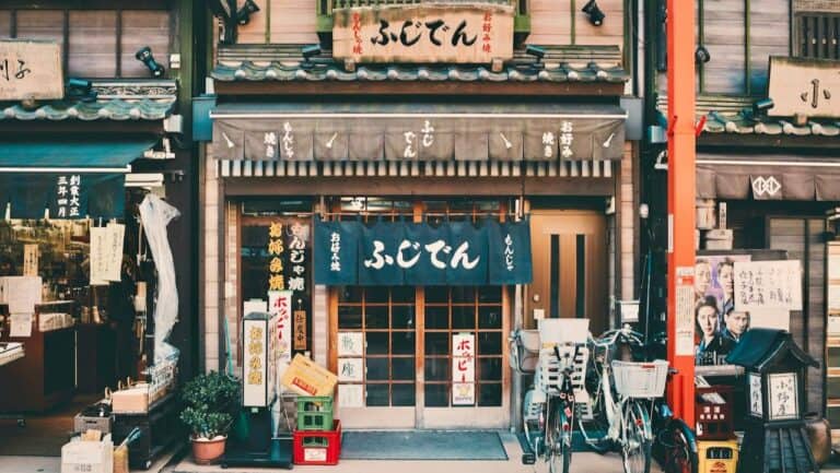 Traditional Japanese shopfront with noren curtains, bicycles, and signage.