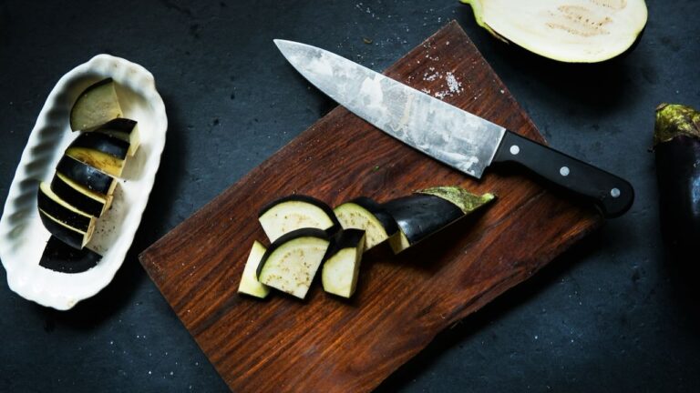 Sliced eggplant on a wooden cutting board with a chef's knife, ready for cooking.
