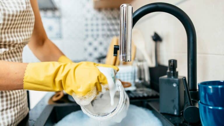 Person washing dishes with yellow gloves in a well-organized kitchen.